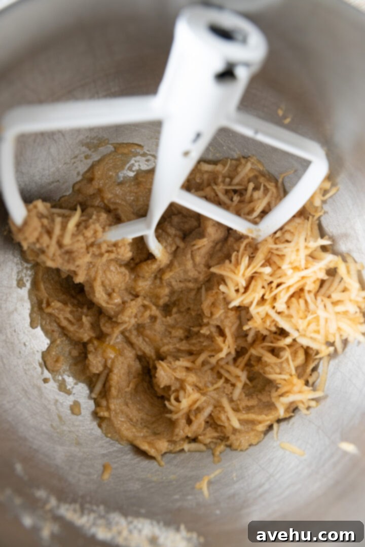 Maple-Glazed Autumn Apple Bites 5 Grated apple added to creamed butter and sugar in a mixing bowl.