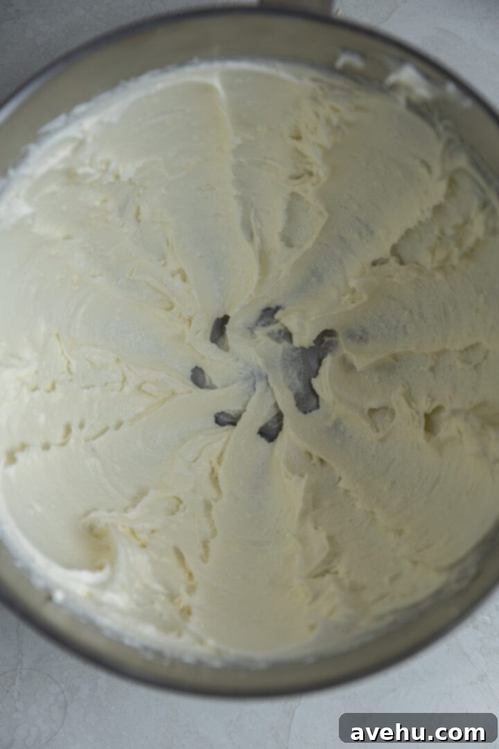 Effortless Cream Cheese Frosting No Powdered Sugar 5 Granulated sugar, vanilla extract, and a pinch of salt mixing into the creamed cream cheese and butter in a bowl, creating a smooth frosting base.