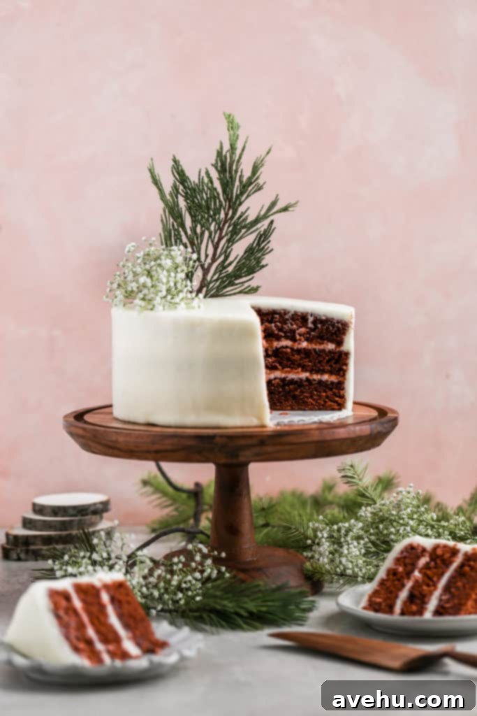 Effortless Rich Red Velvet Cake 2 Cream cheese frosted red velvet cake decorated with leaves on a wood cake stand on a pink background.
