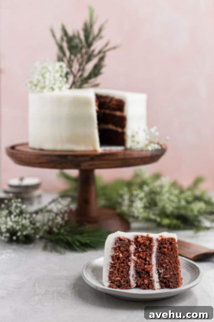 Effortless Rich Red Velvet Cake 3 Cream cheese frosted easy red velvet cake decorated with leaves on a wood cake stand on a pink background.