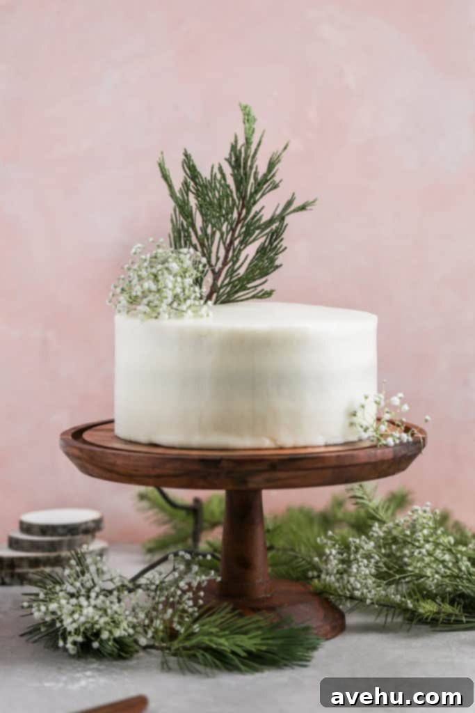 Effortless Rich Red Velvet Cake 5 Cream cheese frosted red velvet cake decorated with leaves on a wood cake stand on a pink background.