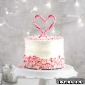 A peppermint cake on a white cake stand surrounded by fairy lights.
