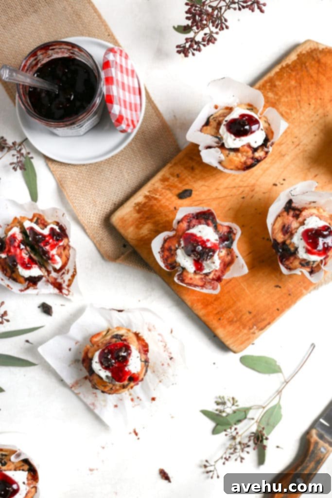 Nutty Butter Dark Cherry Chocolate Muffins 3 A rustic cutting board holds several fluffy cherry muffins, some topped with a generous dollop of whipped cream and extra cherry preserves, showcasing their vibrant color and texture.