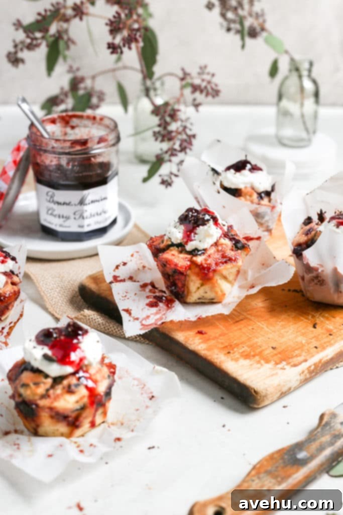 Nutty Butter Dark Cherry Chocolate Muffins 5 A close-up shot of a single, perfectly golden-brown cherry muffin resting delicately on a stack of white ceramic plates. In the background, an open jar of Bonne Maman Cherry Preserves stands ready, its vibrant contents suggesting the delicious filling within the muffin.