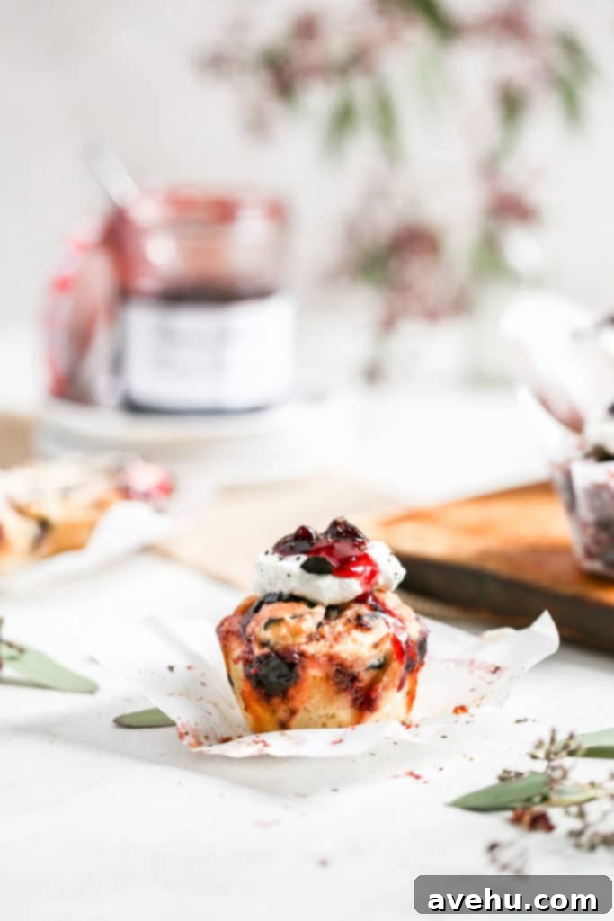 Nutty Butter Dark Cherry Chocolate Muffins 6 A single, perfectly baked cherry muffin is presented on a stack of clean white plates, with an open jar of Bonne Maman Cherry Preserves in the soft background, emphasizing the key ingredient.