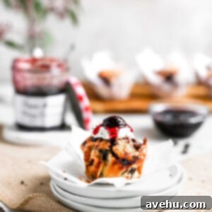Nutty Butter Dark Cherry Chocolate Muffins 7 A single cherry muffin sits atop a stack of white plates, with a vibrant open jar of Bonne Maman Cherry Preserves in the soft background, highlighting the key ingredient.