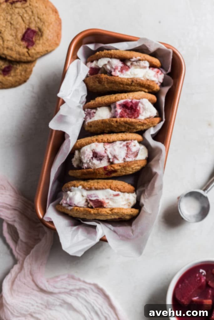 Tangy-Sweet Rhubarb Strawberry Ice Cream Sandwiches 2 Stacked rhubarb ice cream sandwiches, revealing creamy vanilla ice cream swirled with vibrant pink strawberry rhubarb, nestled between soft, chewy cookies in a loaf pan.