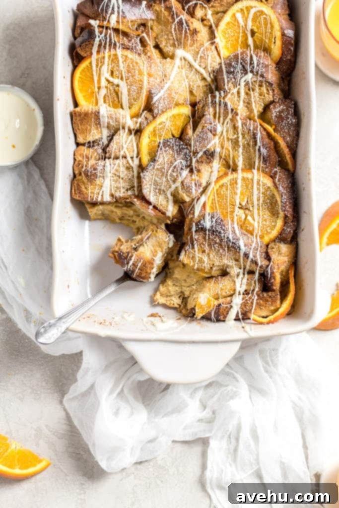Overnight Golden Challah French Toast Bake 2 A spoon dipping into a baked casserole with challah and oranges and drizzled with white chocolate