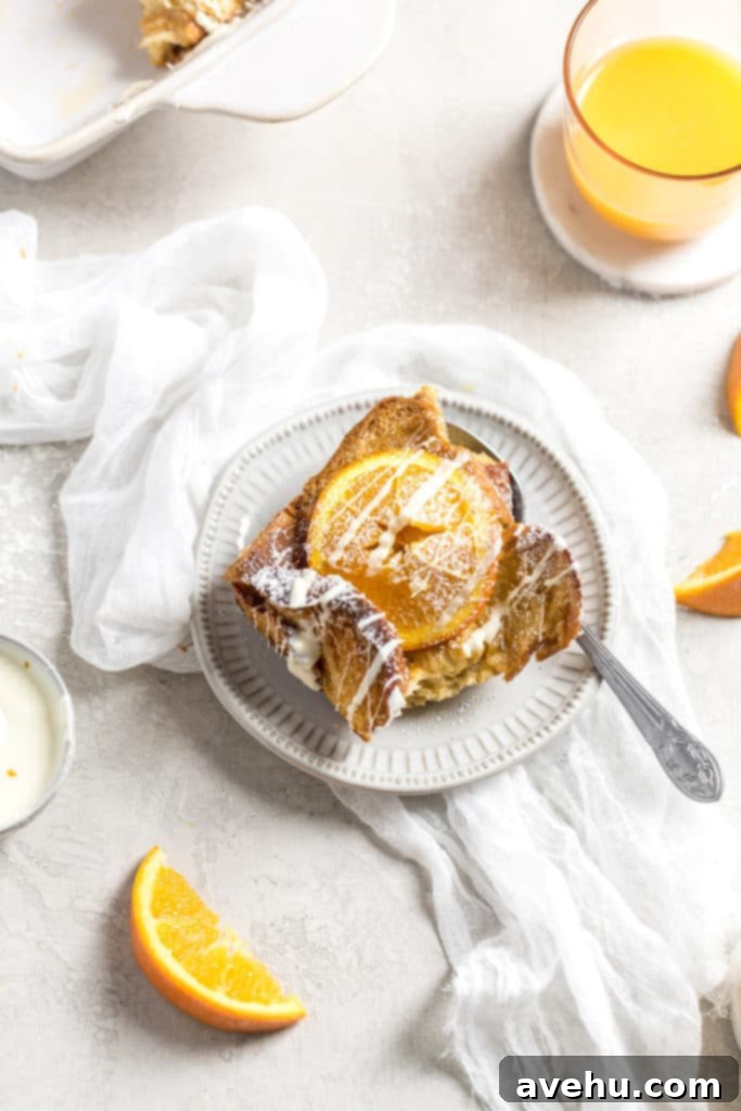 Overnight Golden Challah French Toast Bake 4 A serving of challah French toast with and orange on top on a plate with orange juice in a cup in the background