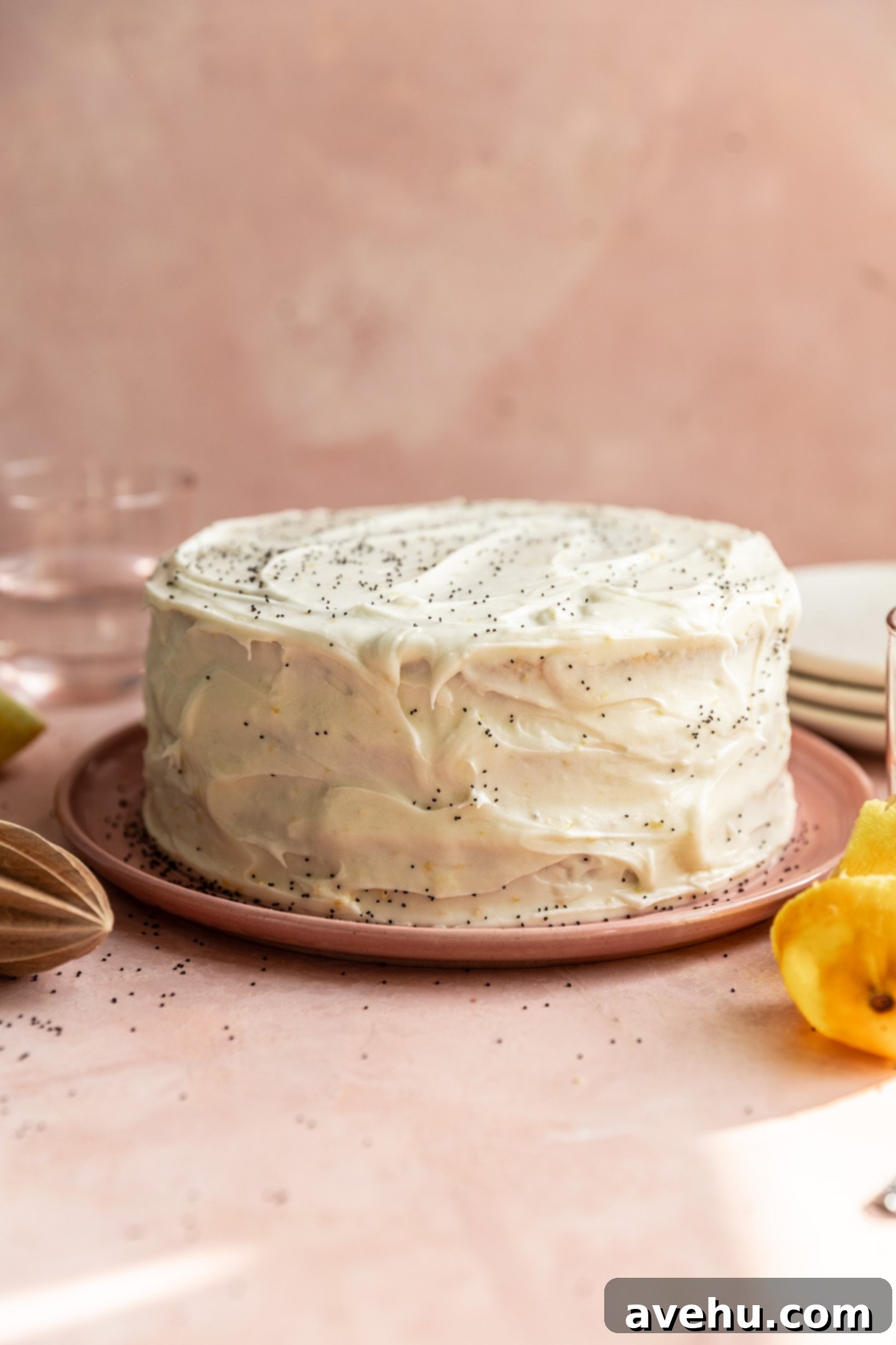 Sunshine Lemon Poppyseed Yogurt Layer Cake 2 A beautifully decorated three-layer lemon poppy seed cake on a pink plate, topped with lemon cream cheese frosting and sprinkled with poppy seeds.