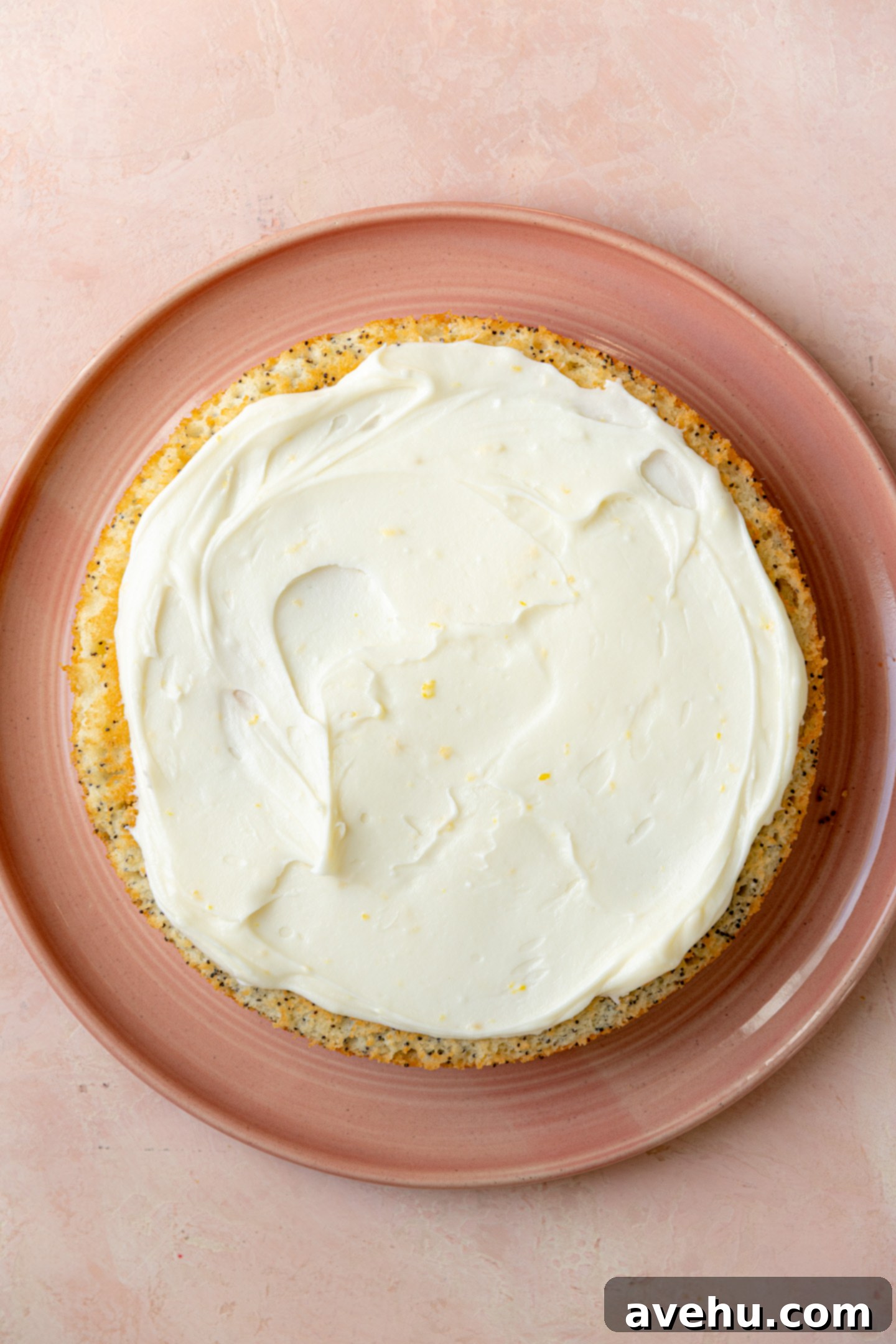 Sunshine Lemon Poppyseed Yogurt Layer Cake 12 A single layer of lemon poppy seed cake on a pink plate, generously topped with white lemon cream cheese frosting.