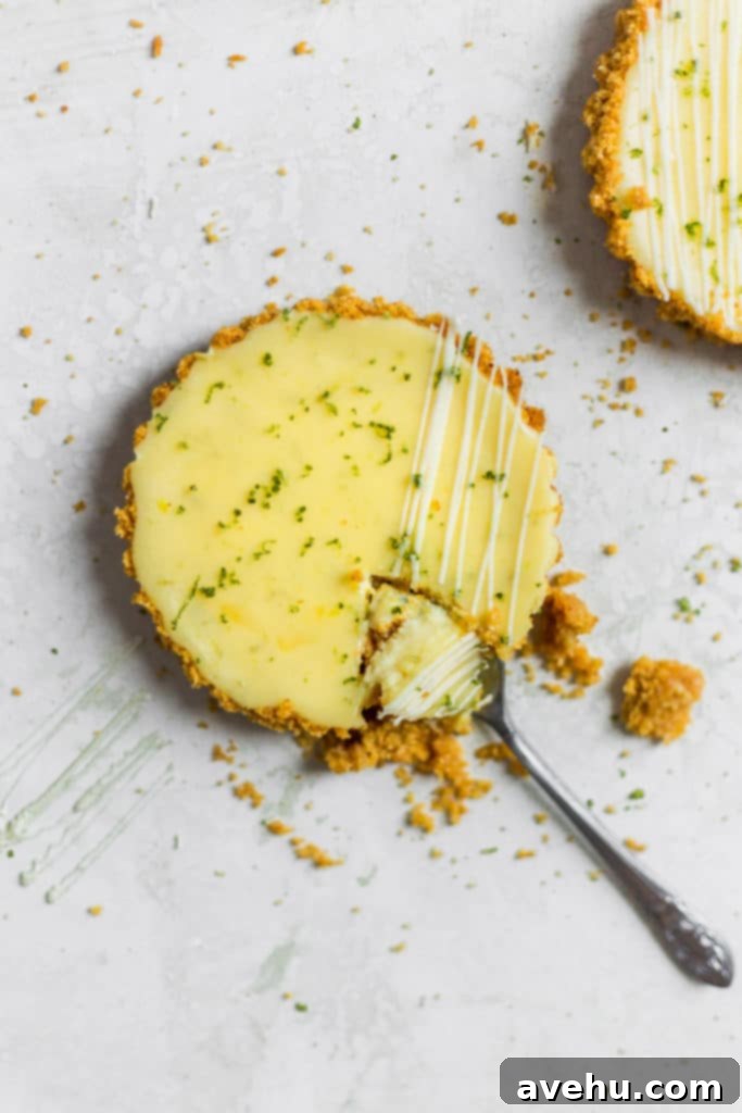 Foolproof Key Lime Pie 5 A spoon digging into a mini key lime pie, showing its soft custard filling and crisp graham cracker crust.