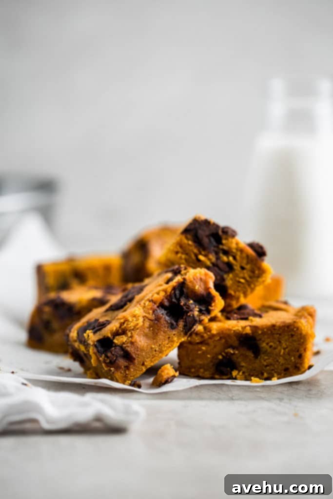 Pumpkin Chocolate Chunk Delights 3 Close-up of freshly baked pumpkin bars with melted chocolate chunks, cooling on parchment paper, with a glass of milk in the soft background, evoking a cozy autumn scene.