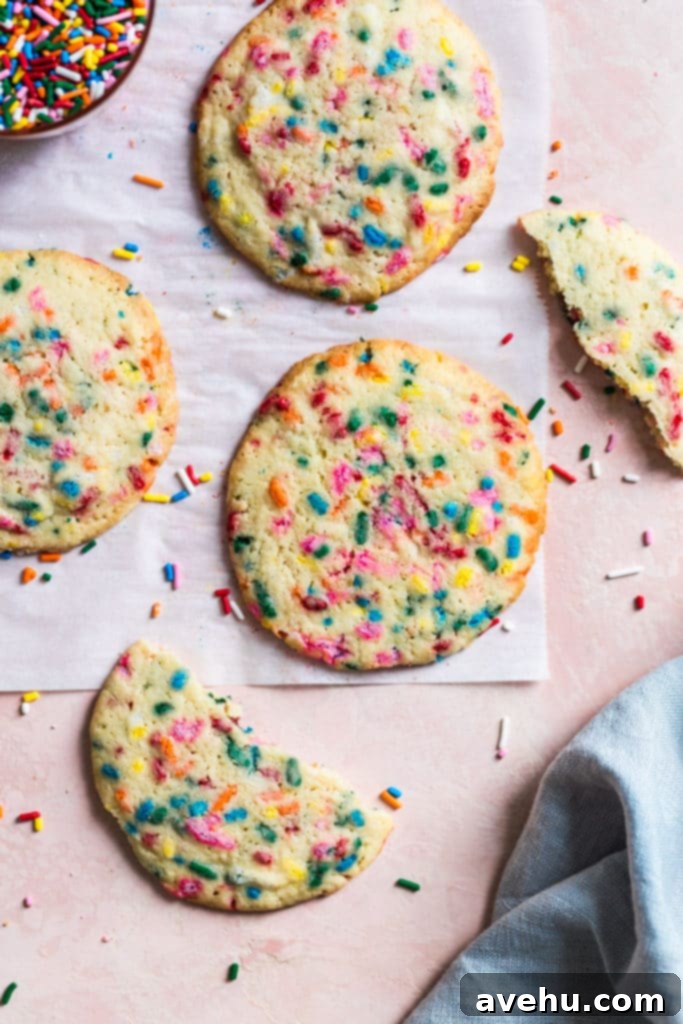 Scratch Baked Funfetti Delights 2 Freshly baked homemade funfetti cookies with abundant sprinkles on parchment paper on a pink background