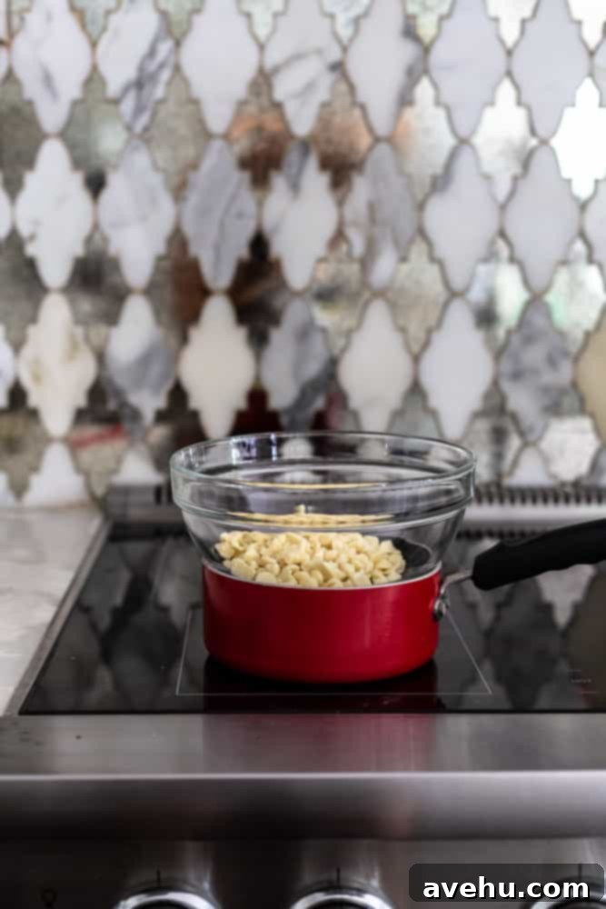 Effortless and Perfectly Moist Blackberry Cake 7 A glass bowl of white chocolate chips on top of a pot on a stove, demonstrating how to set up a double boiler.