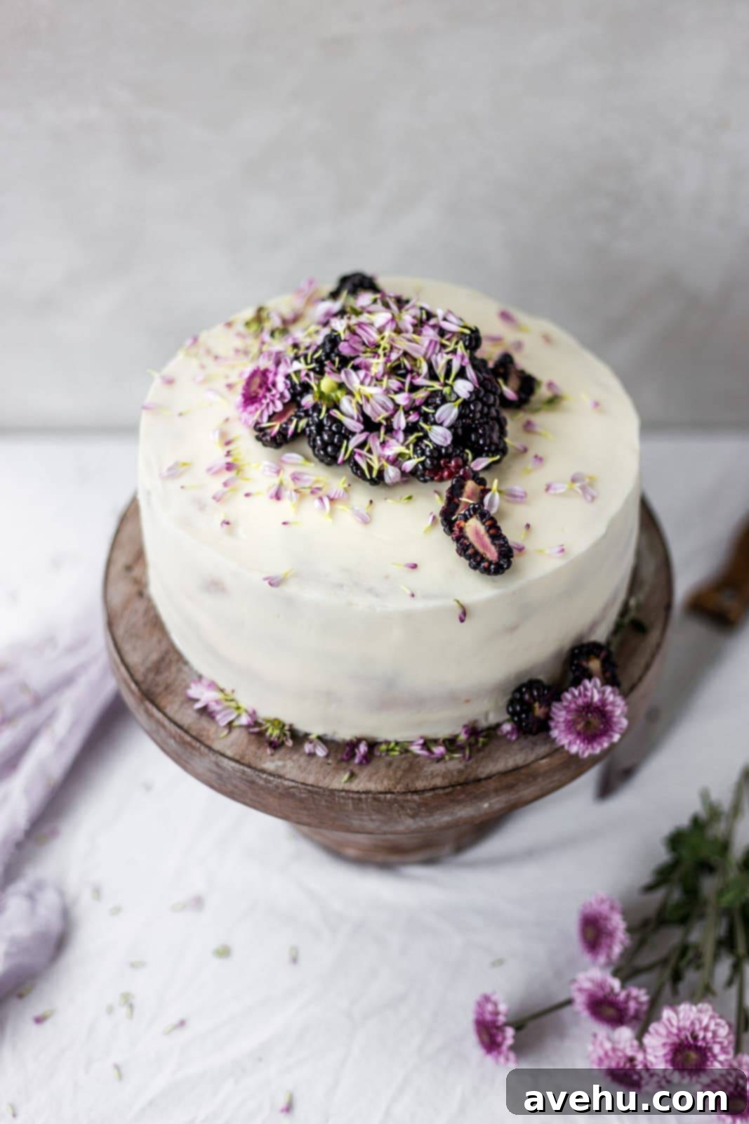 Effortless and Perfectly Moist Blackberry Cake 9 The top of a white cake with fresh blackberries and purple flowers, beautifully decorated.