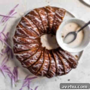 A sliced apple bundt cake with white glaze drizzled, next to a bowl of glaze.