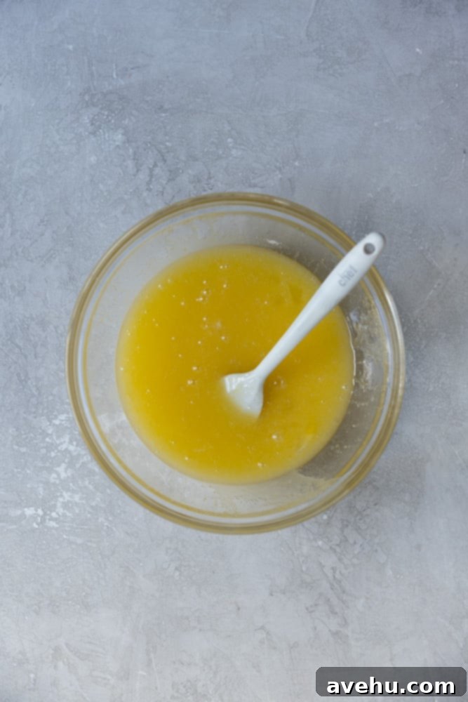 Irresistible Gooey One Bowl Blondie Cookies 2 Melted butter, granulated sugar, and large eggs mixed thoroughly in a clear glass bowl, showing a frothy, pale yellow mixture.