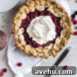 Cranberry pie with whipped cream resting on a white linen on a gray backdrop with a knife lying on an angle.