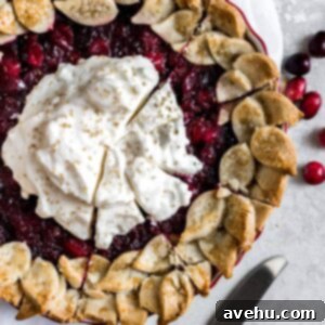 A closeup of a cranberry pie topped with whipped cream that has slices cut into it.