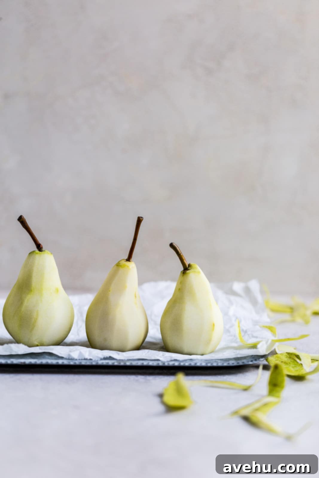 Sweet Pear Streusel Delight 3 Three peeled Anjou pears arranged neatly on a tray with parchment paper, ready for poaching.