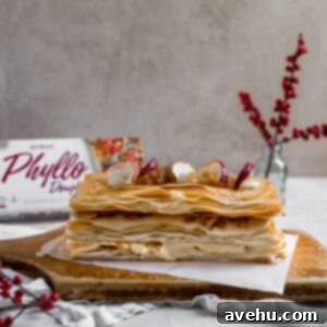 A Napoleon dessert made with phyllo dough on a wooden cutting board topped with dried apples and red flower berries in the background.