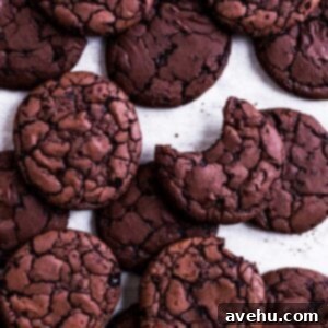 Close-up of a stack of fudgy chocolate brownie cookies on parchment paper, highlighting their crinkly tops.