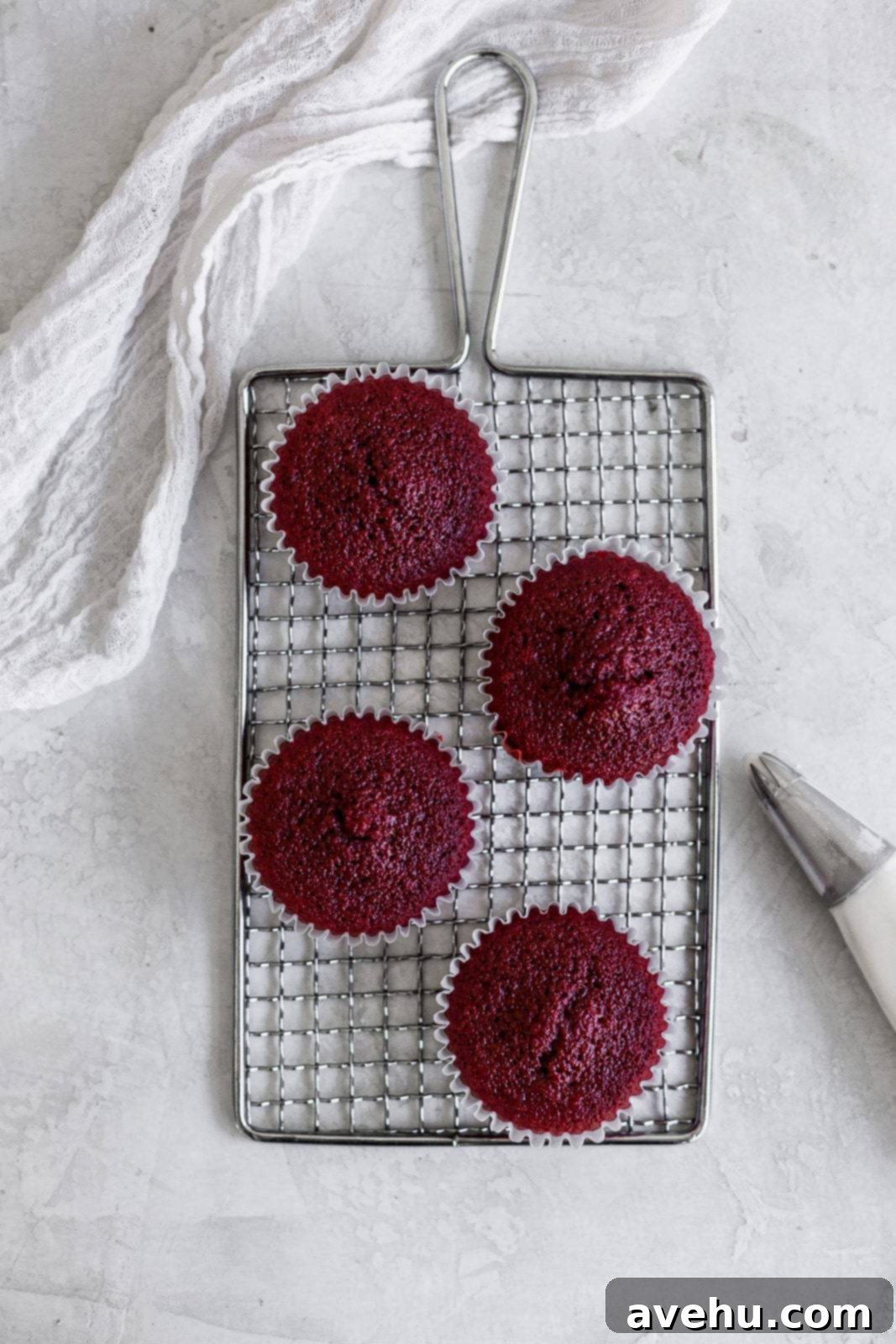 Scarlet Velvet Cheesecake Delights 3 Four perfectly baked red velvet cheesecake cupcakes cooling on a small wire rack against a gray background, showcasing their fluffy texture.