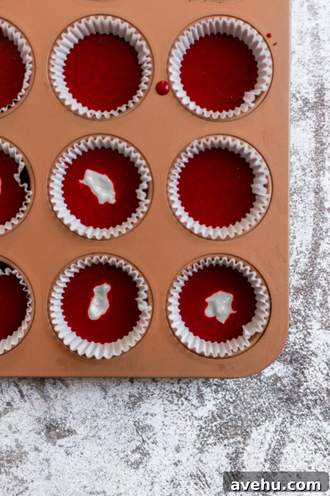 Scarlet Velvet Cheesecake Delights 4 An orange cupcake tin lined with white cupcake liners, half-filled with vibrant red velvet cupcake batter, ready for the cheesecake filling.