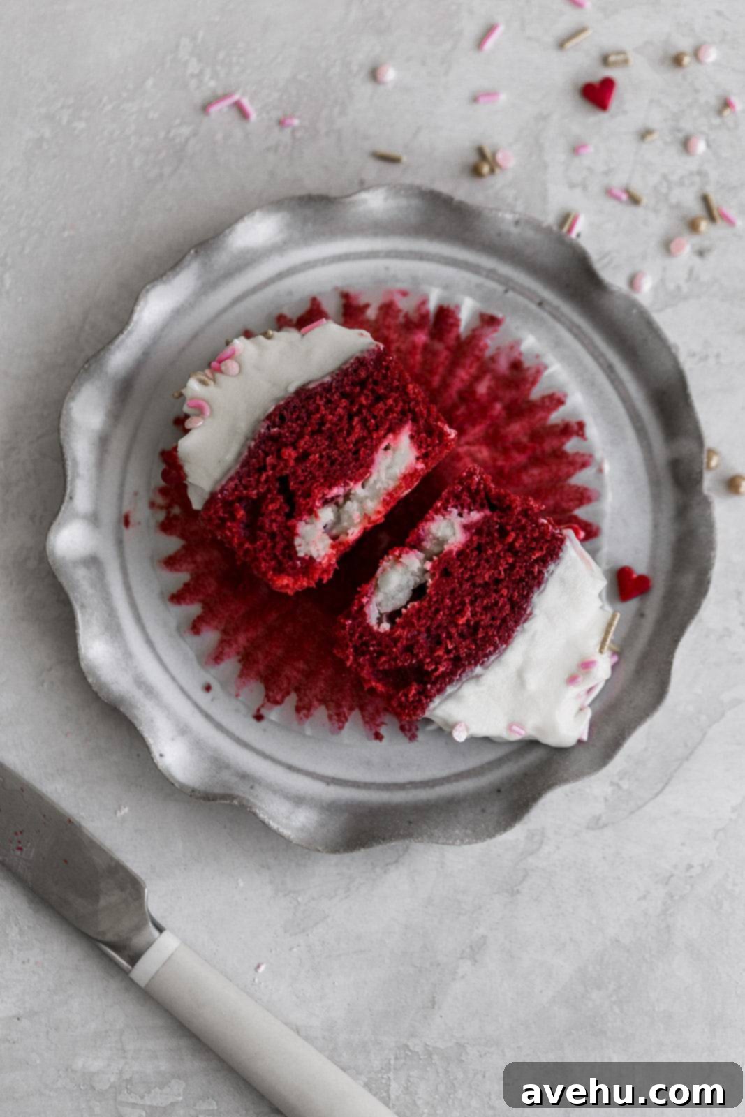 Scarlet Velvet Cheesecake Delights 5 A red velvet cupcake cut in half, revealing its creamy cheesecake filling inside, elegantly presented on a gray plate.