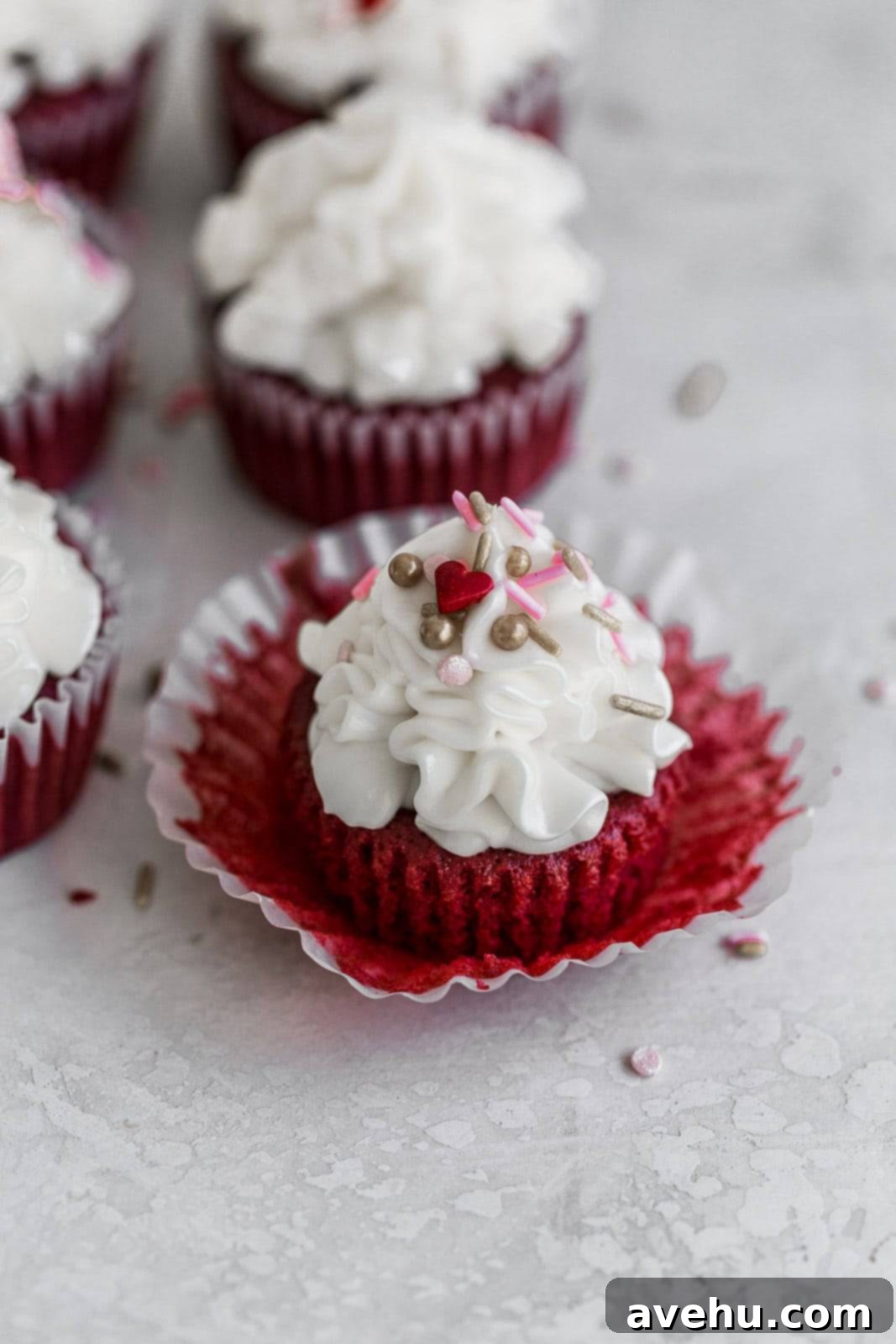 Scarlet Velvet Cheesecake Delights 7 A beautifully presented red velvet cheesecake cupcake, adorned with cream cheese frosting and colorful sprinkles, sitting in an open liner on a white surface, inviting a delicious bite.