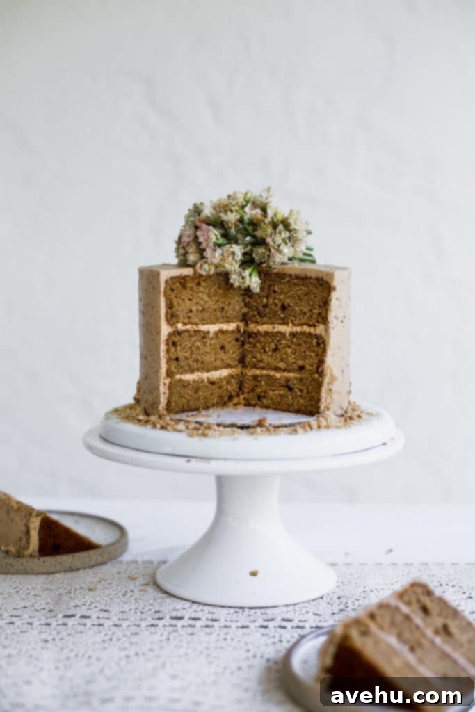 Irresistible Cookie Butter Dream Cake 2 A brown cake with beige frosting that has a few slices taken out of it sitting on a white cake stand on a white background