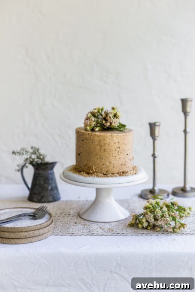 Irresistible Cookie Butter Dream Cake 3 A brown cake with pink flowers on top sitting on a white cake stand on a table with candlesticks and a vase of flowers