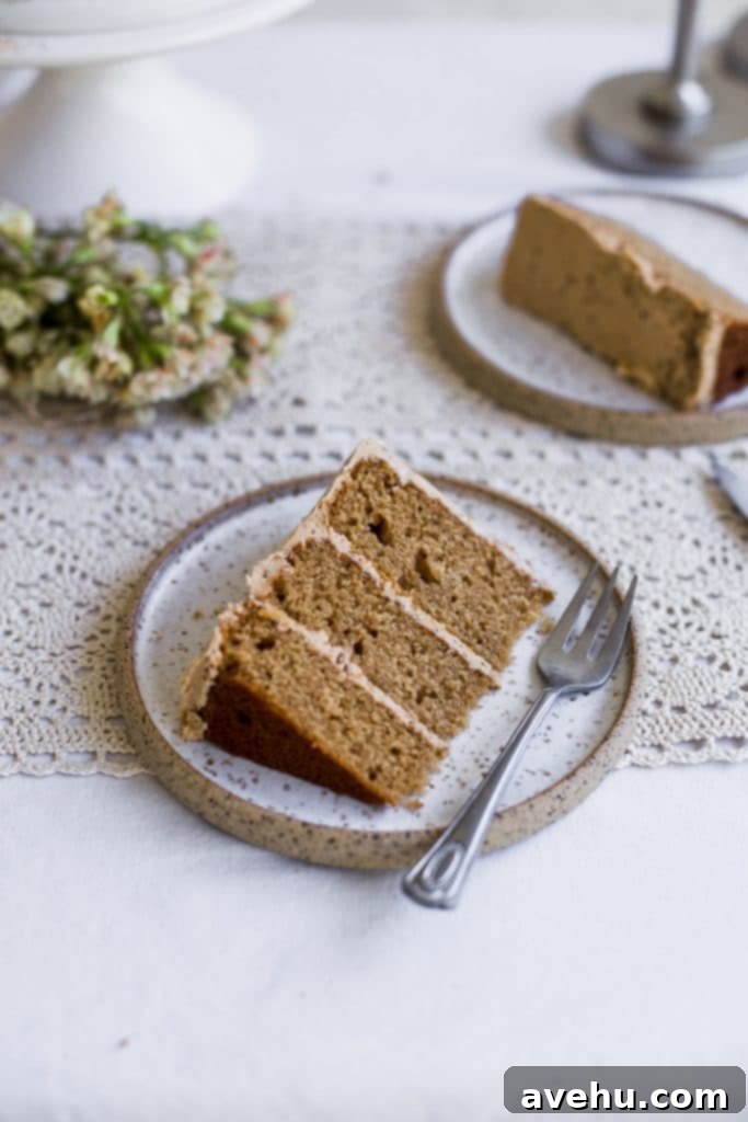 Irresistible Cookie Butter Dream Cake 4 A slice of 3 layer cakes with beige frosting on a white plate with a fork sitting next to it. Styled on an eyelet tablecloth