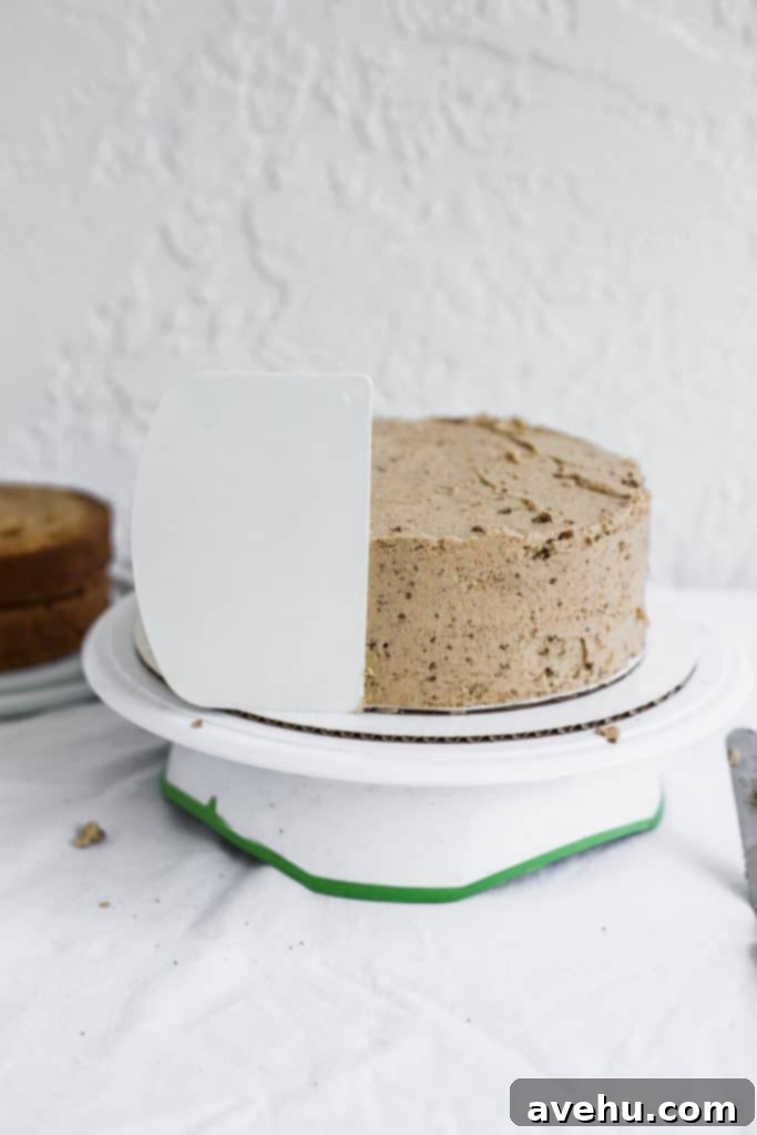 Mastering Two-Tier Cakes: Baking and Stacking Techniques 15 A white bench scraper sticking to the side of a beige frosted cake