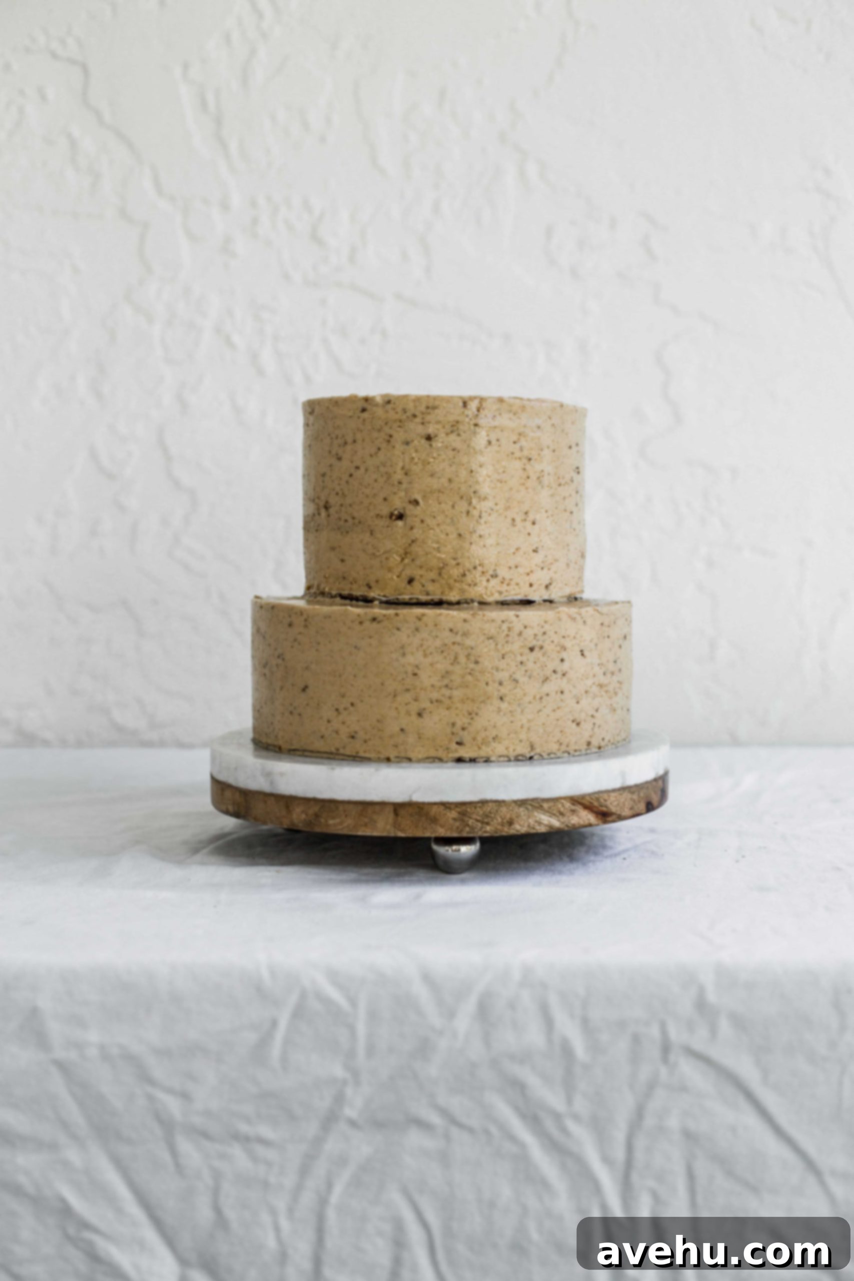 Mastering Two-Tier Cakes: Baking and Stacking Techniques 23 a two tier stacked beige cake sitting on a marble and wood cake plate
