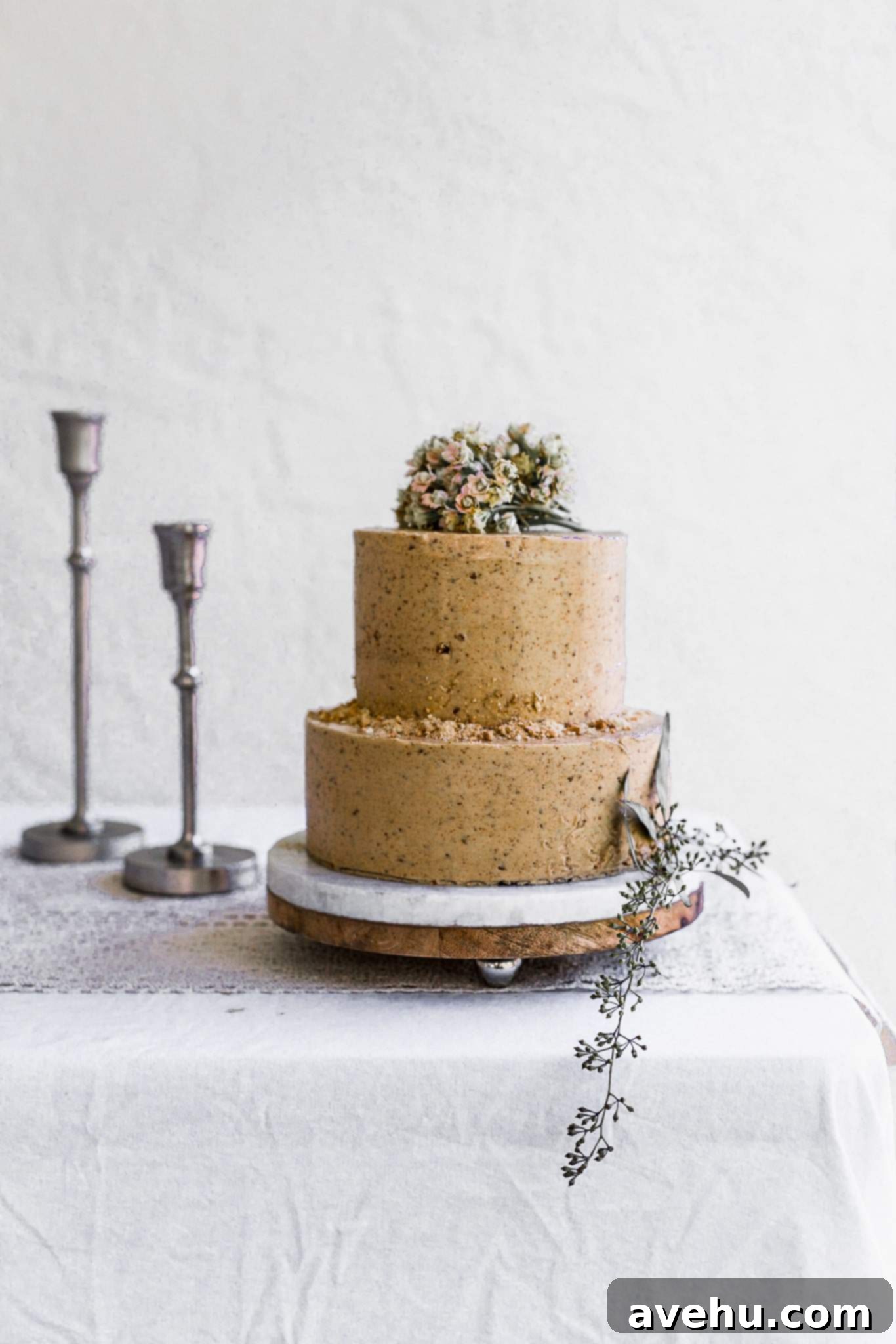 Mastering Two-Tier Cakes: Baking and Stacking Techniques 24 A two tier brown cake decorated with flowers and cookie crumbs sitting on a white table with silver candlesticks in the back