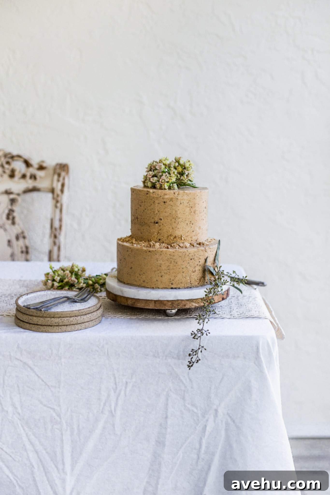 Mastering Two-Tier Cakes: Baking and Stacking Techniques 25 A two tier brown cake decorated with flowers and cookie crumbs sitting on a white table with plates and forks on the side.
