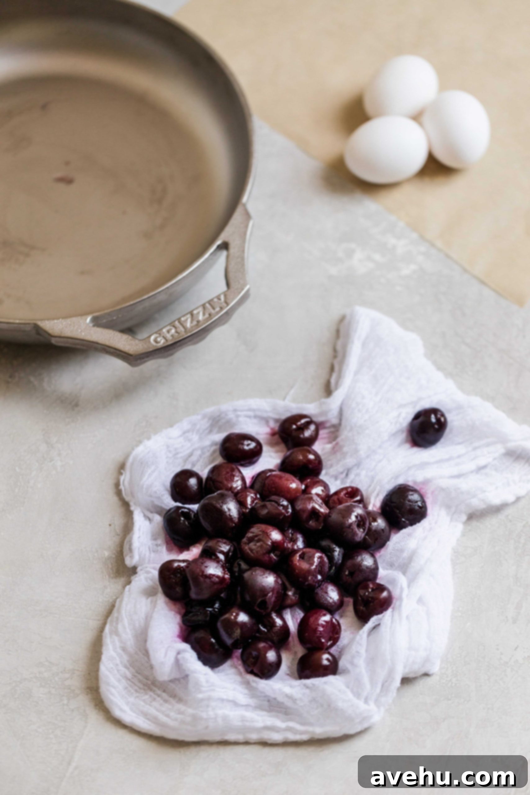Bourbon Cherry Clafoutis 4 Frozen thawed cherries drying on a white cheesecloth on a grey background.