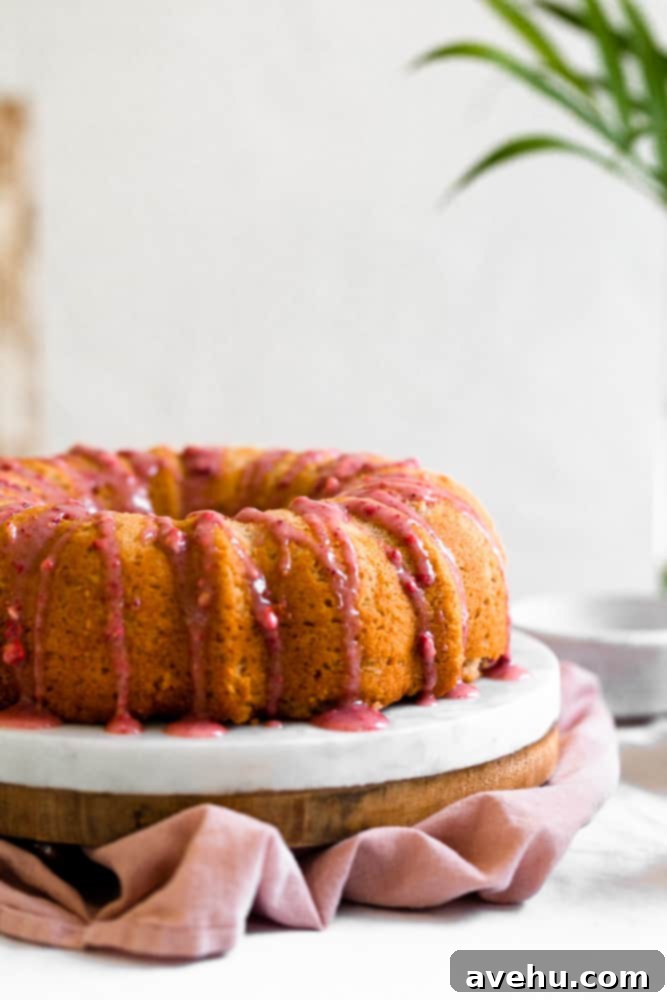 Luscious Strawberry Bundt Cake 2 A vibrant pink strawberry glaze gracefully dripping down a freshly baked bundt cake, presented on a pristine white surface, highlighting its moist texture and rich color.