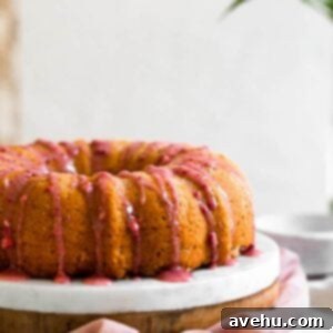 Luscious Strawberry Bundt Cake 5 A beautifully baked bundt cake, adorned with a luscious pink strawberry glaze dripping down its sides, presented invitingly on a white surface.