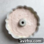 Luscious Strawberry Bundt Cake 8 Rich strawberry cake batter evenly fills a bundt pan, sitting on a gray surface, ready for baking to achieve its beautiful shape.