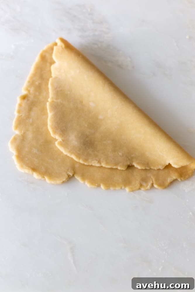 Layers of Perfection: Flaky Pie Crust 12 A delicate pie crust, gently folded over itself in half on a white surface, demonstrating the preparation for transfer to a pie pan.
