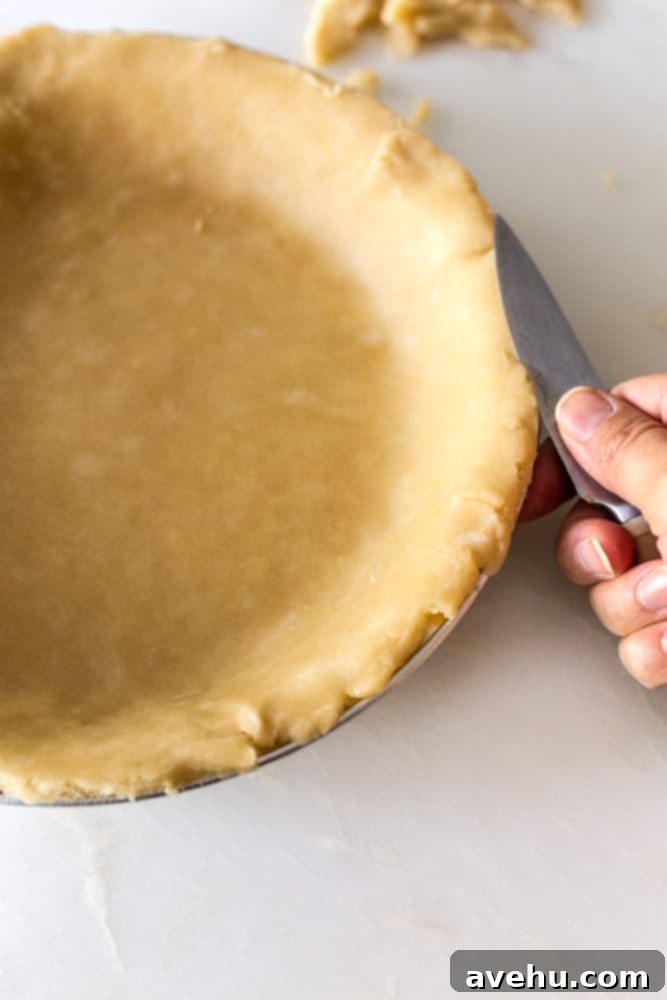 Layers of Perfection: Flaky Pie Crust 15 A sharp knife carefully trimming the excess edges of a flaky pie crust in a metal pan, creating a neat and defined border.