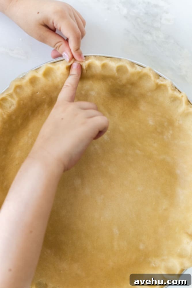 Layers of Perfection: Flaky Pie Crust 16 A close-up of hands expertly crimping the edges of a pie crust with fingers, demonstrating the technique to create a decorative, finished look.