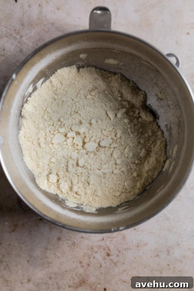 Layers of Perfection: Flaky Pie Crust 5 A close-up view of the flour, butter, and shortening mixture in a metal mixing bowl, showcasing the pea-sized crumbs after the fats have been cut in, indicating proper consistency.