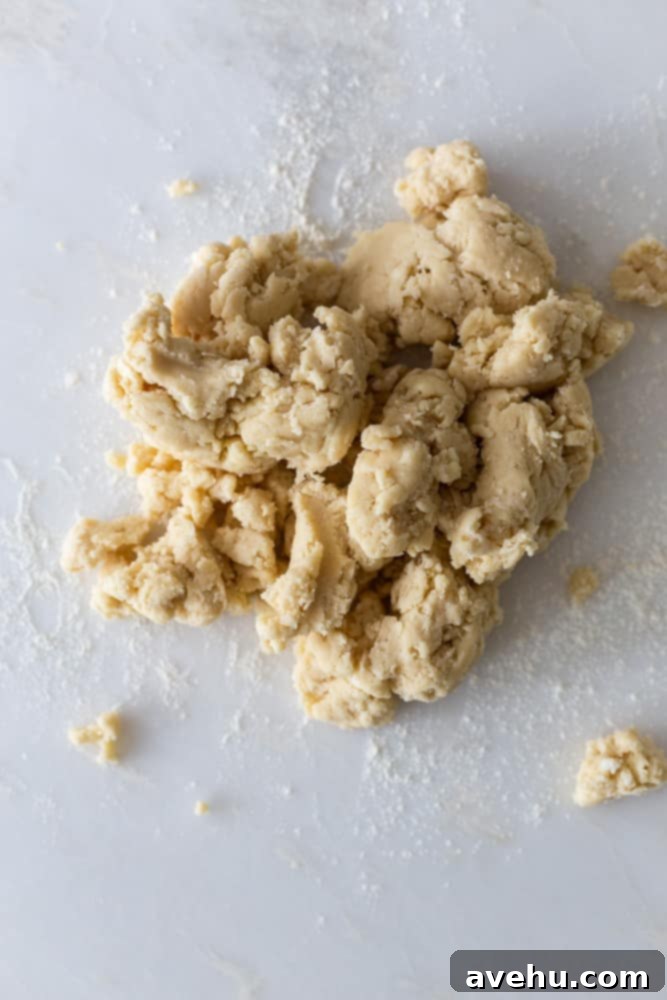 Layers of Perfection: Flaky Pie Crust 7 Shaggy pie dough pieces on a lightly floured white surface, demonstrating the texture after mixing but before full consolidation.