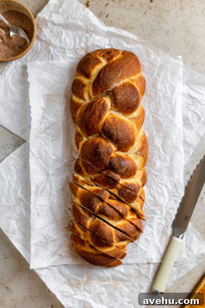 Homemade Challah Perfection 2 A beautiful 6-strand challah braid, freshly baked and sliced, revealing its soft, fluffy interior, resting on a clean white surface. The cinnamon sugar topping is visible.