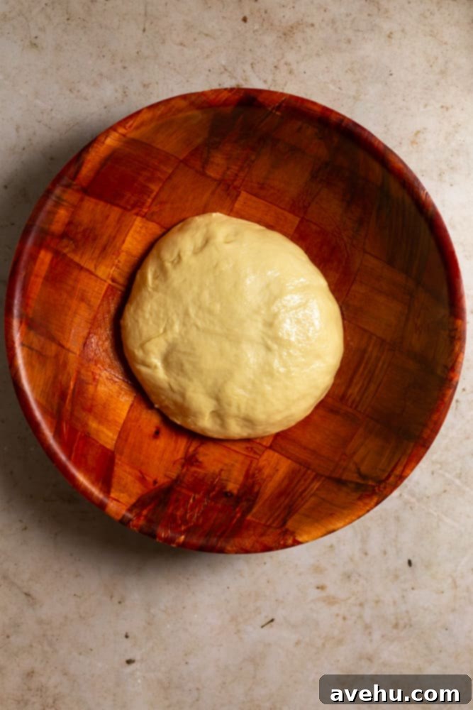 Homemade Challah Perfection 8 Flattened challah dough coated with oil in a wooden bowl, covered and ready for its first rise.