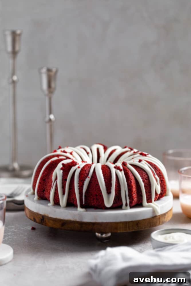 Decadent Fluffy and Moist Red Velvet Bundt Cake 2 A stunning, perfectly fluffy and moist red velvet bundt cake on a marble and wood cake stand, drizzled with silky cream cheese frosting, set against a elegant gray surface.